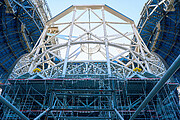 In the centre of the image is a large set of support beams surrounded by smaller blue scaffolding, as the viewer, we are looking up at the centre from below. Blue sky peaks out from behind the support structure where the dome above splits.